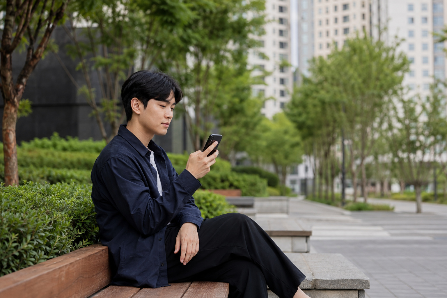 도시의 보행로 벤치에서 청년이 휴대전화를 살펴보는 일상 장면